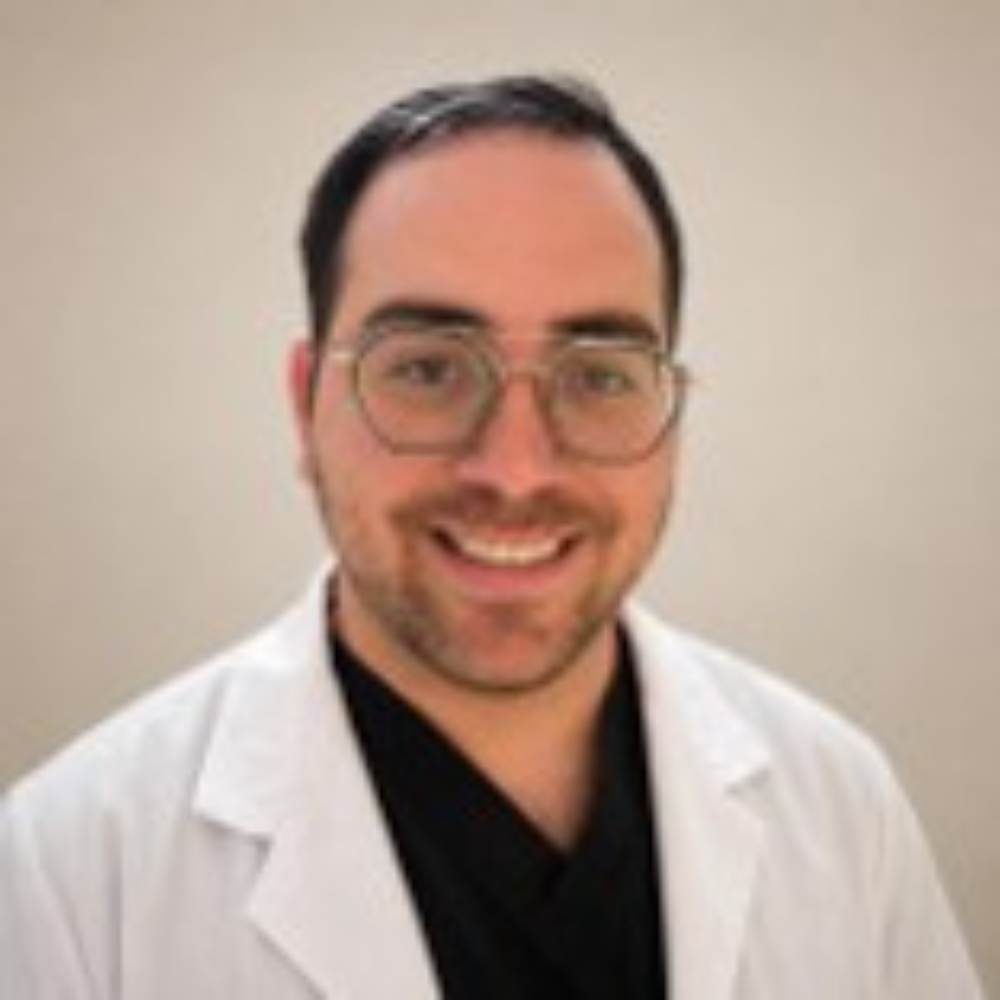 man with short dark hair wearing glasses and white coat