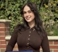 woman with long hair wearing brown top in front of brick wall