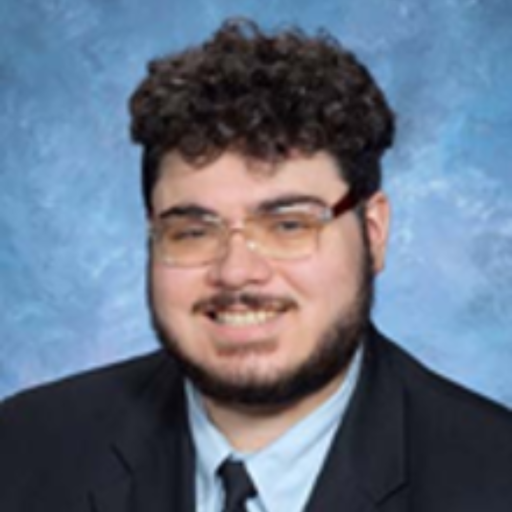 man with dark hair and mustache and beard wearing glasses and dark suit