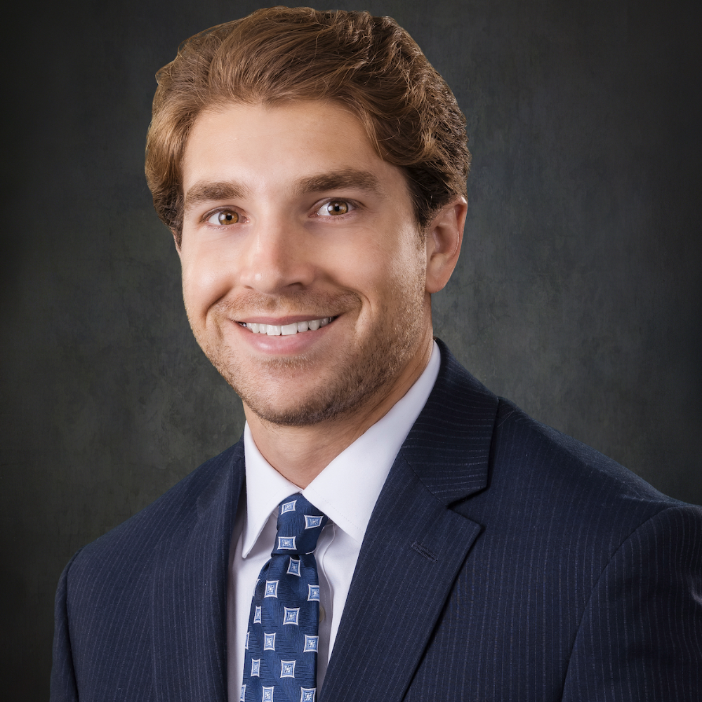 man wearing blue suit and blue tie in front of gray background