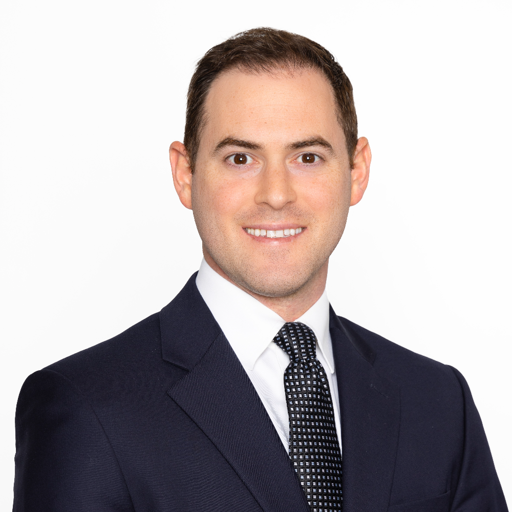 man with short dark hair wearing a suit and tie in front of a white background