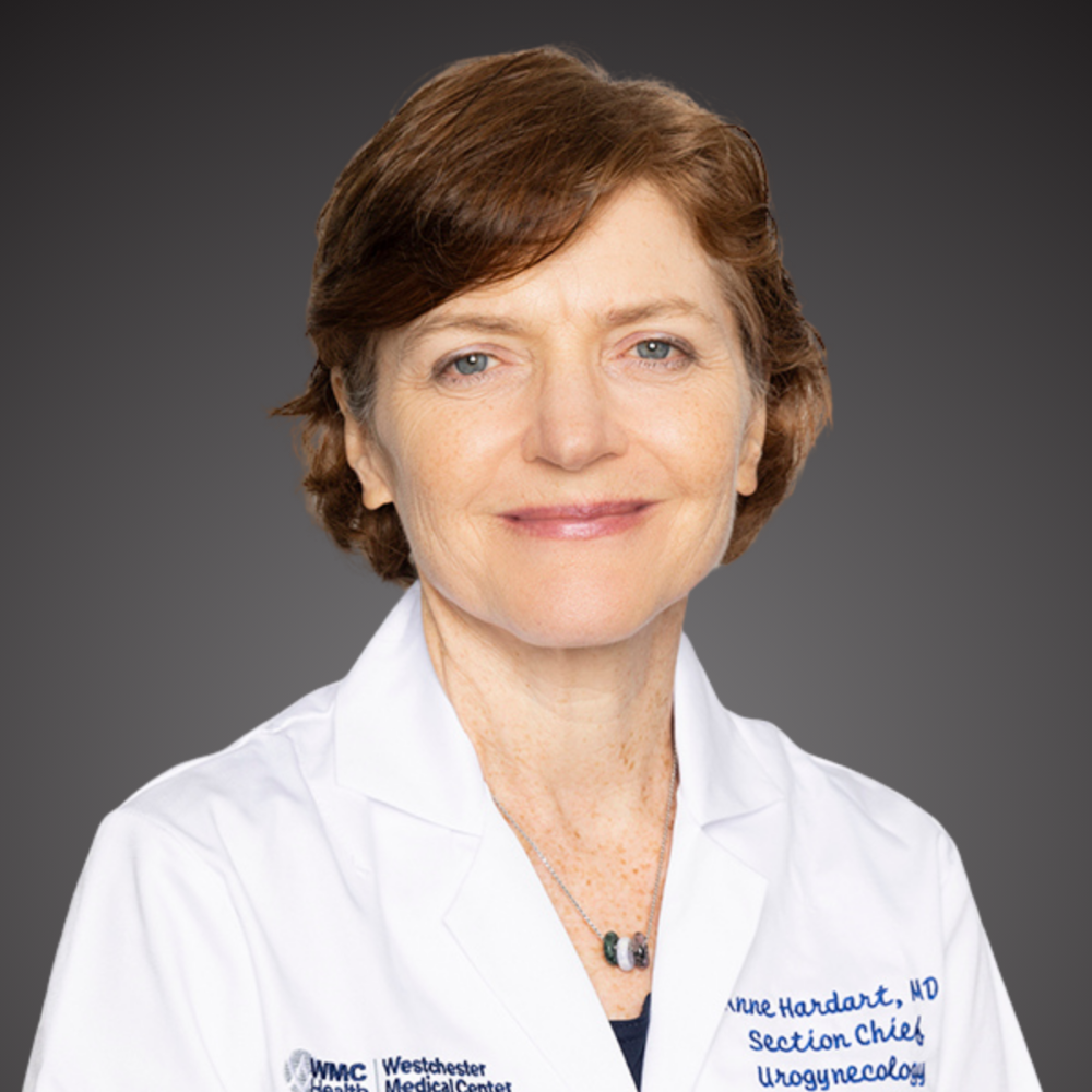 woman with short hair wearing white coat in front of gray background