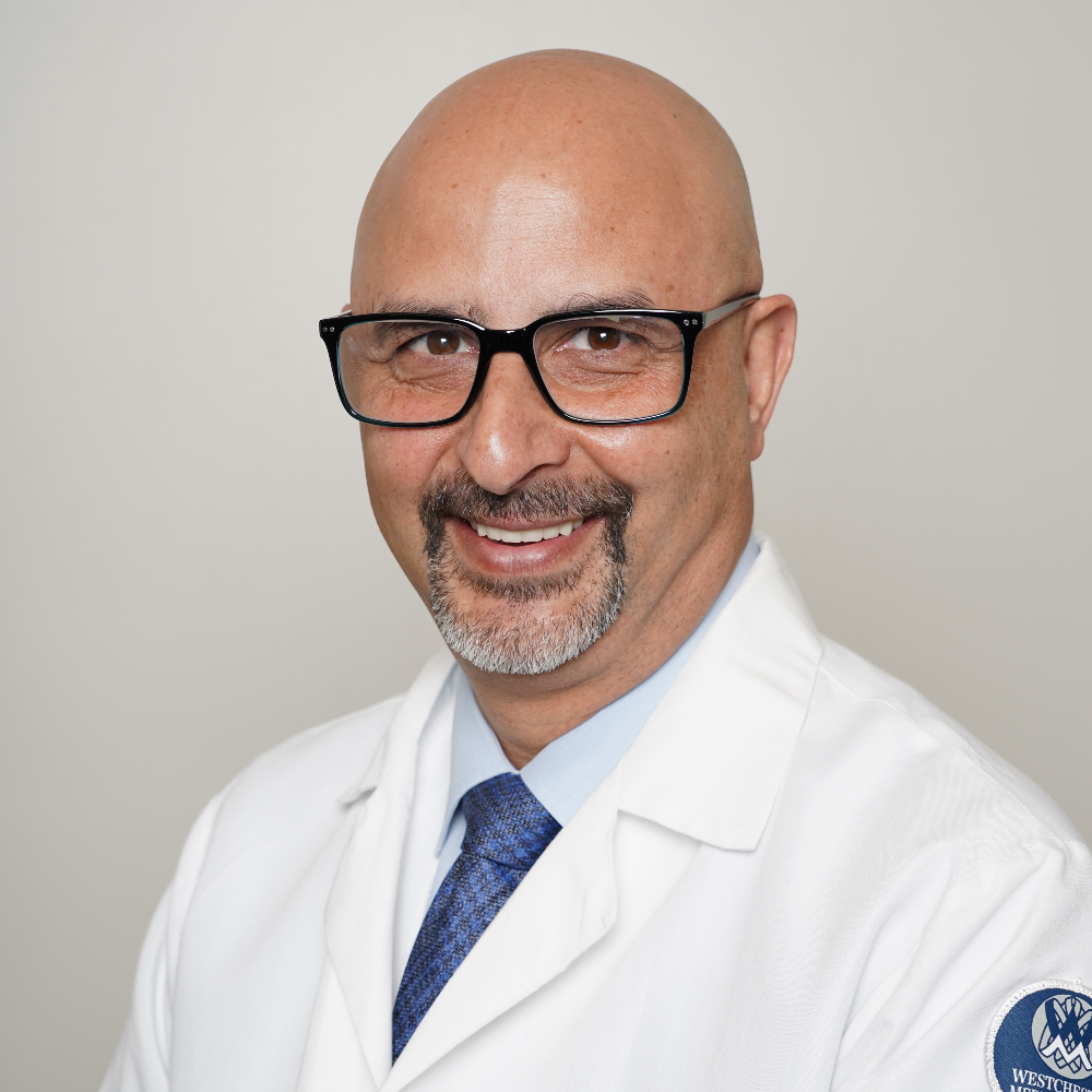 bald man with mustache and beard wearing glasses and white coat in front of light gray background