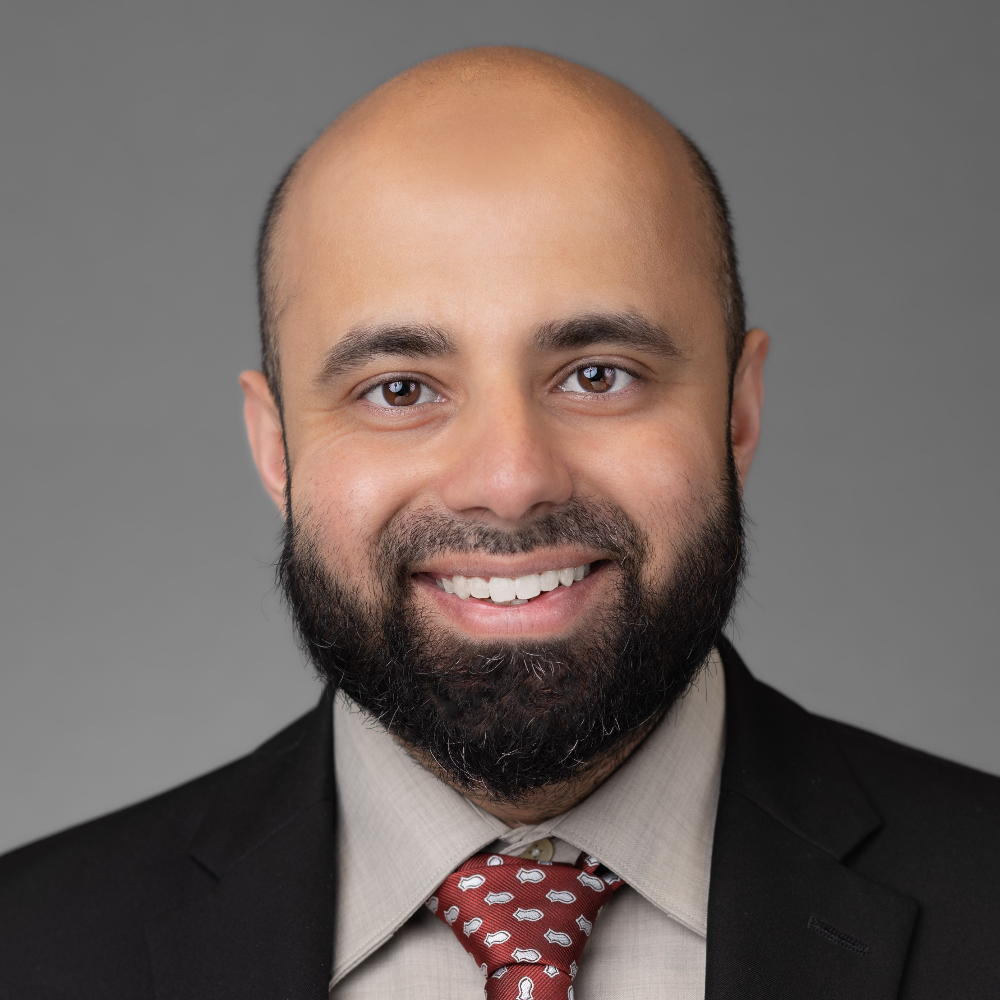 bald man with beard wearing black suit with tan shirt and red patterned tie