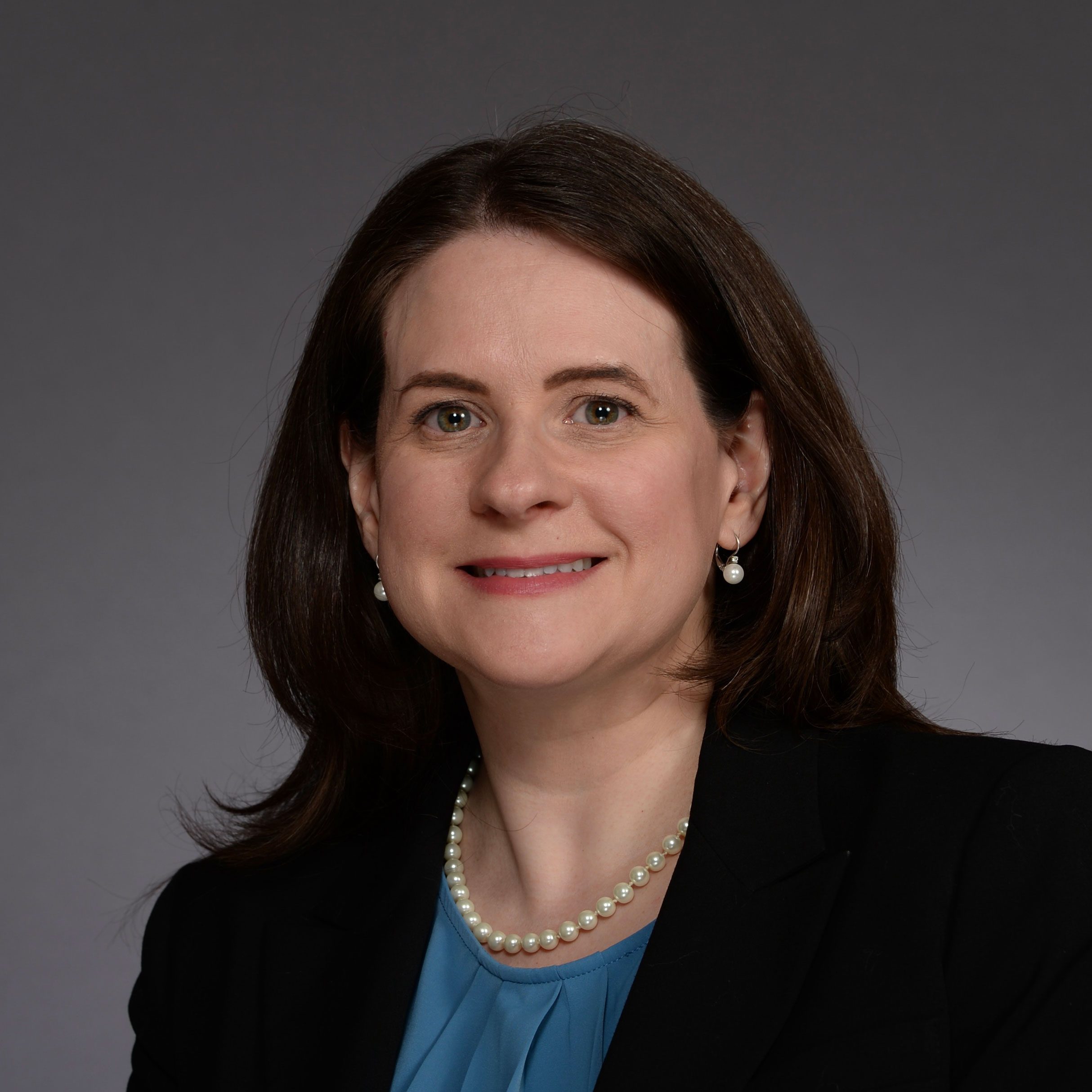 woman with long dark hair wearing dark suit jacket and blue top