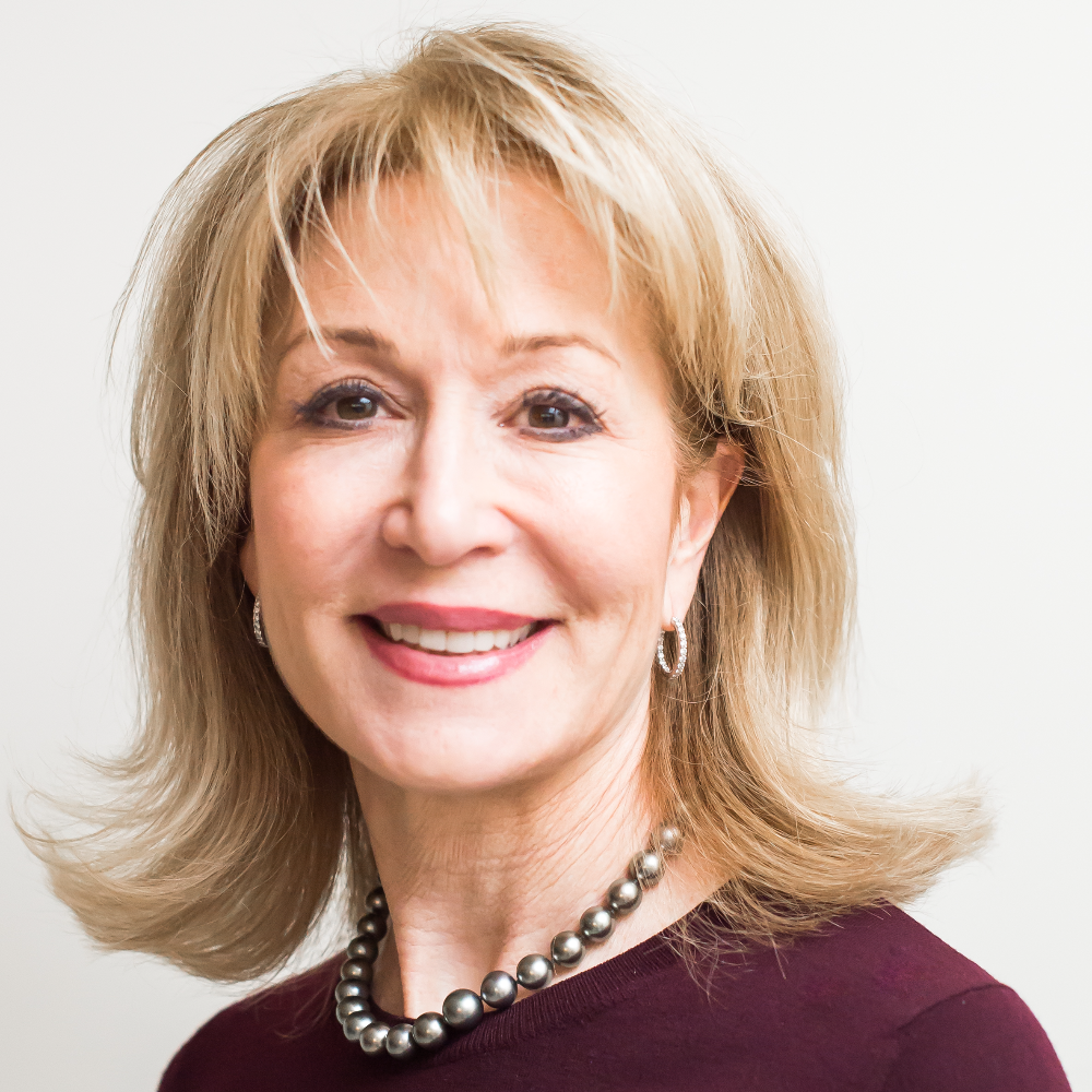 woman with blond hair wearing purple top and gold necklace and earrings
