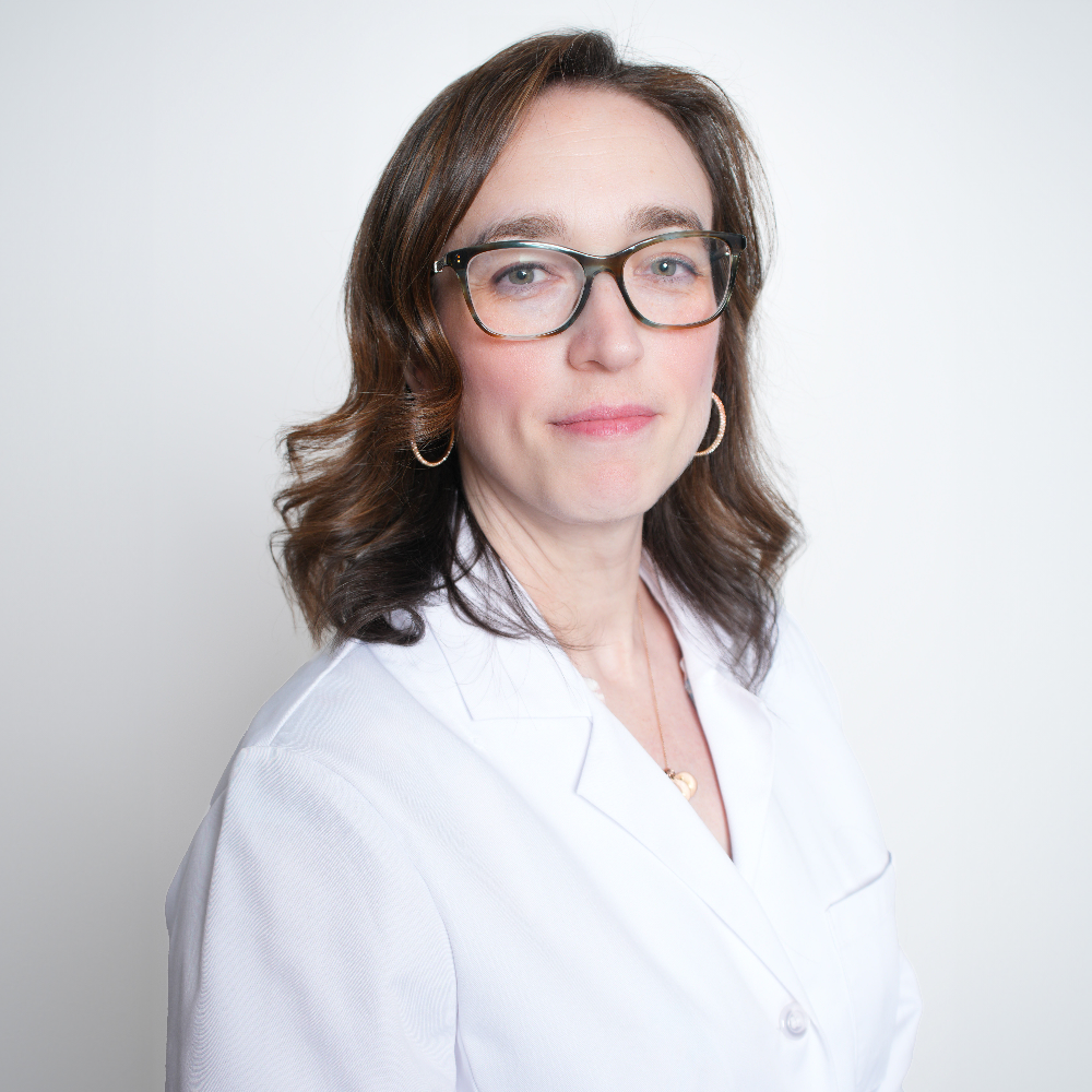 woman with long brown hair and glasses wearing white coat