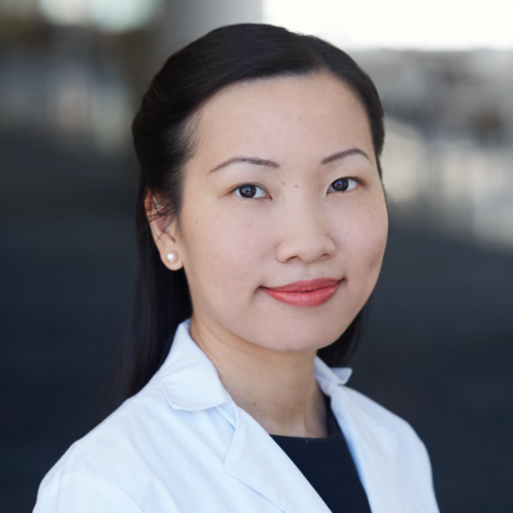 Asian woman with dark hair tied back wearing white coat