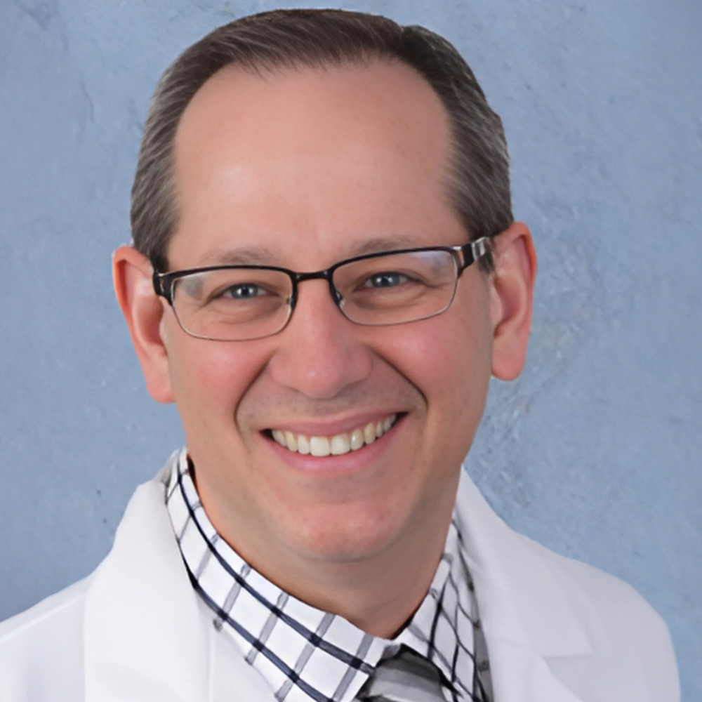 man wearing glasses and white coat in front of blue background