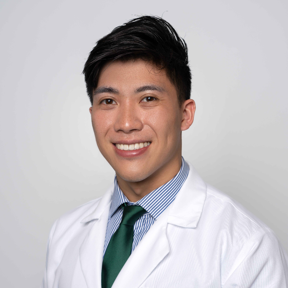 Asian man with short dark hair wearing white coat and blue shirt and tie