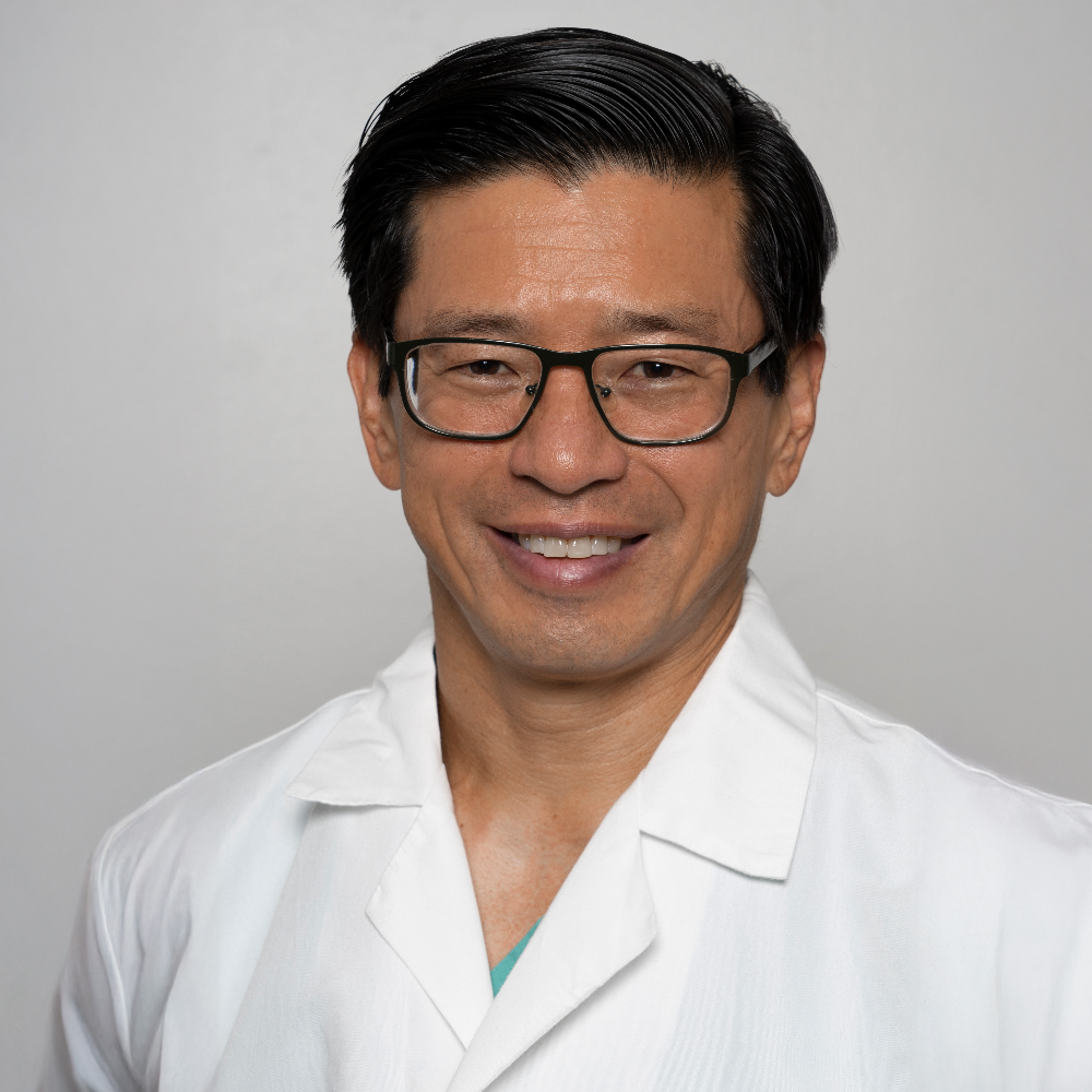 man with short dark hair and glasses wearing white coat