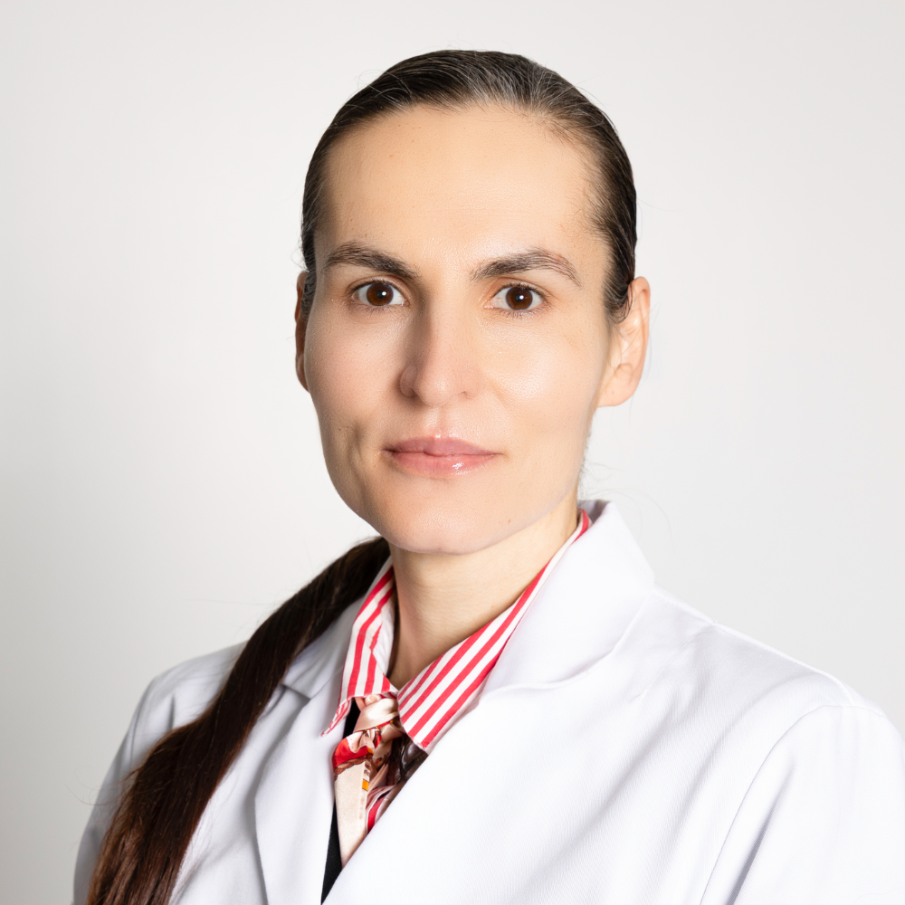 woman with dark hair in pony tail wearing white coat and red shirt