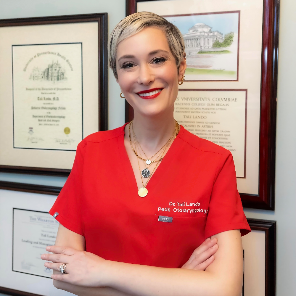 woman with short blond hair with arms crossed wearing red scrubs