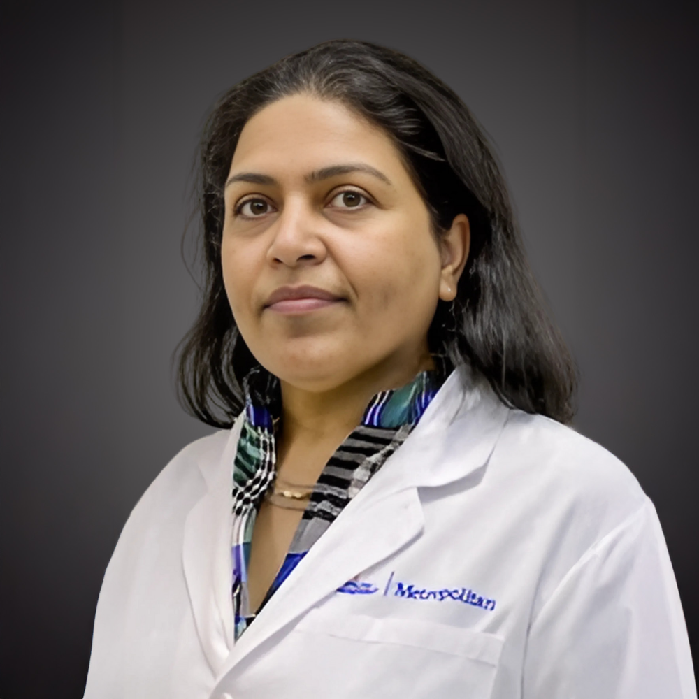 woman with dark hair wearing white coat in front of gray background