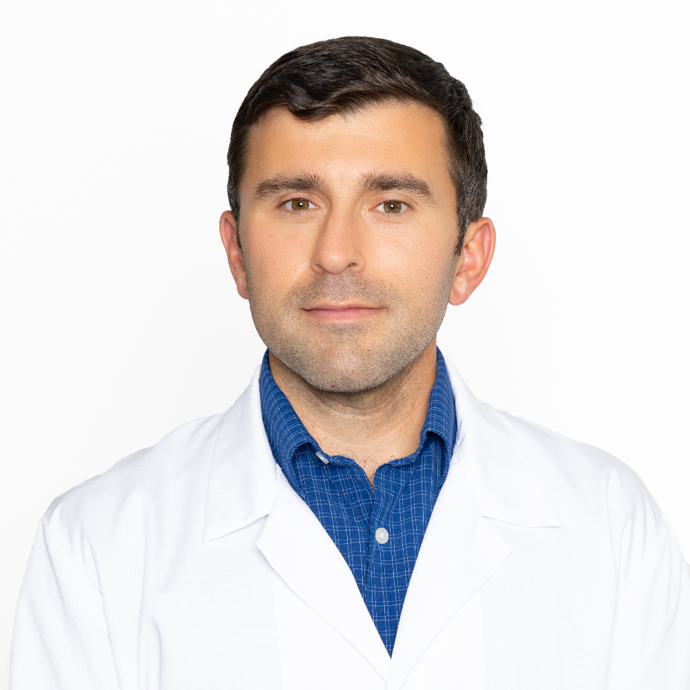 man with short brown hair wearing white coat and blue shirt
