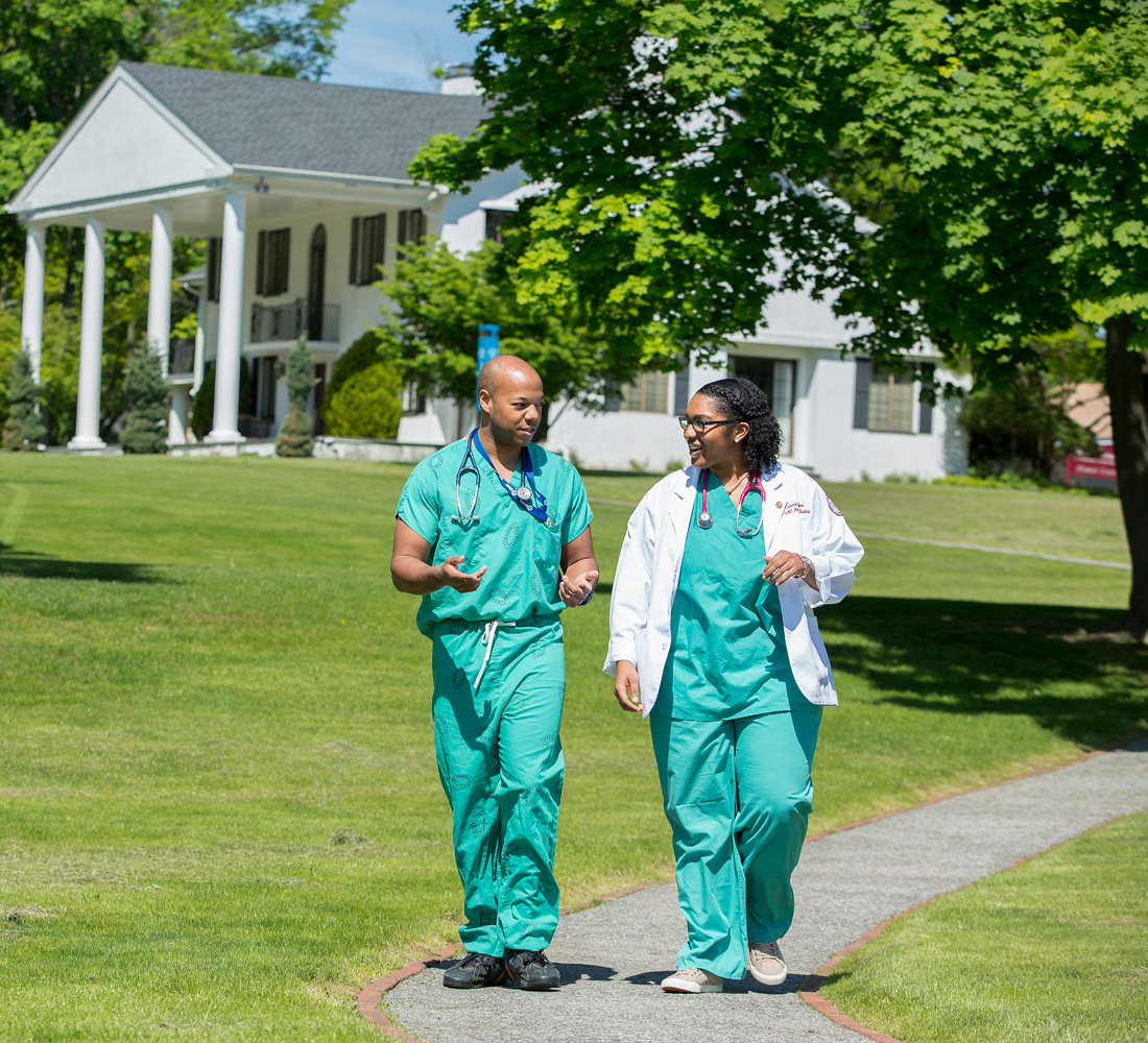 two medical students walking on campus while wearing scrubs