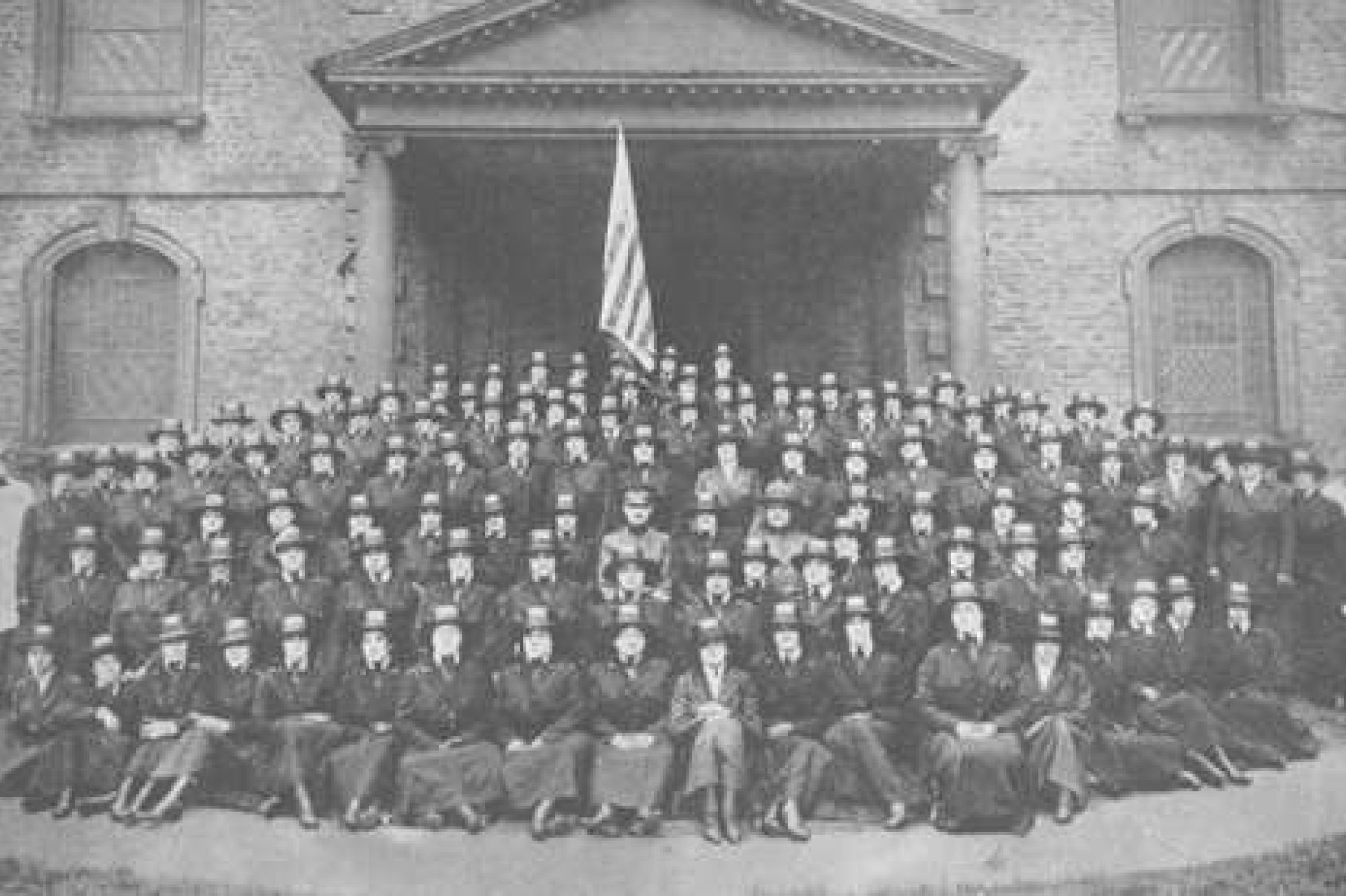 Base hospital 48. Large group of men posing in dark uniform in front of building with American flag hanging overhead