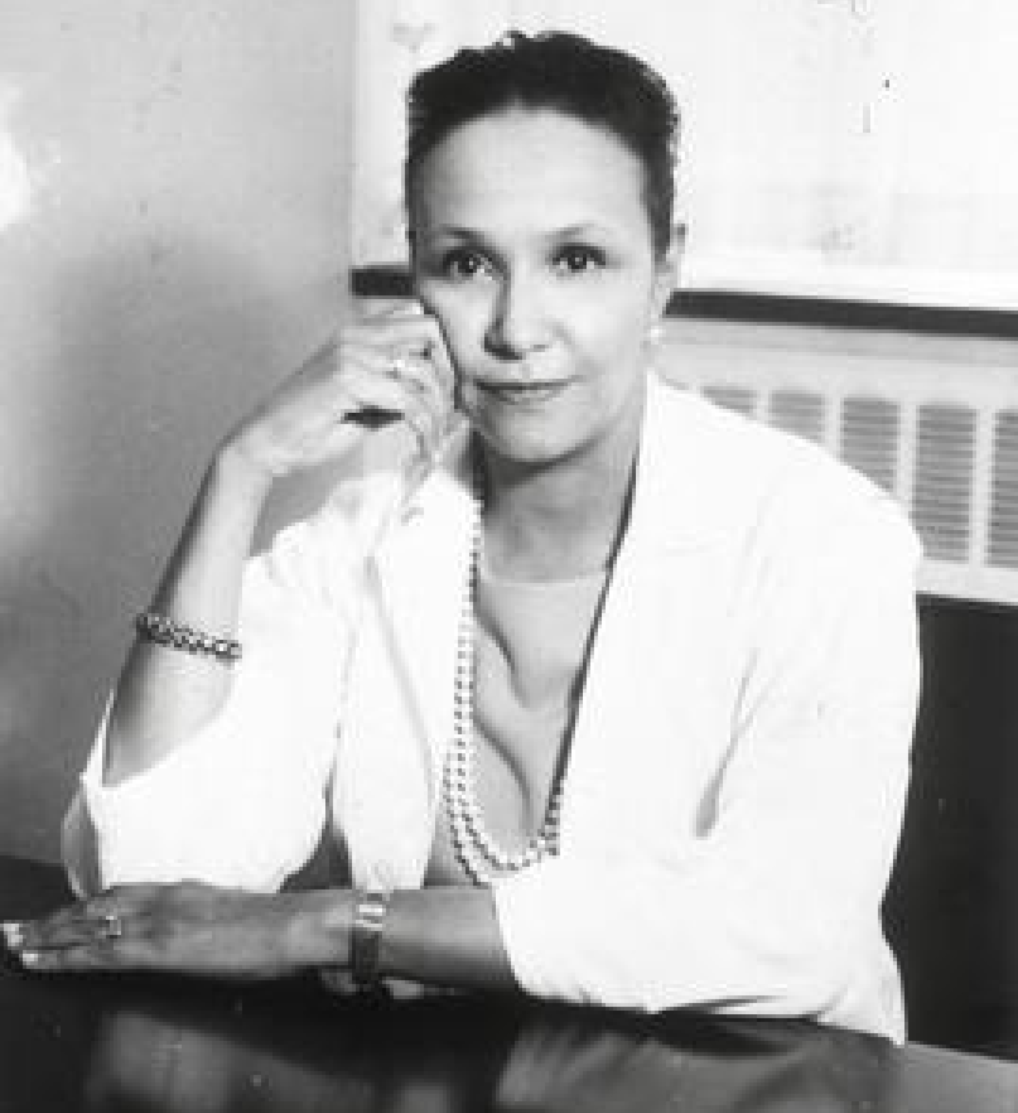 Jane Cooke Wright sitting at desk with dark hair, a soft smile, a white blazer, and a pearl necklace. She is posing with her elbow on the desk and her hand on her cheek.