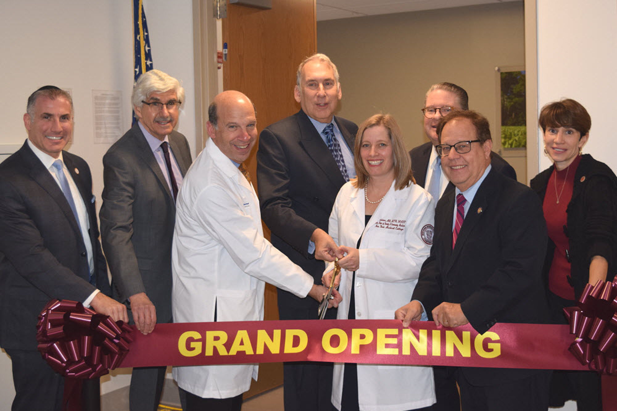 NYMC faculty and administration smiling and excitedly holding large scissors to cut grand opening banner at the family health center grand opening event