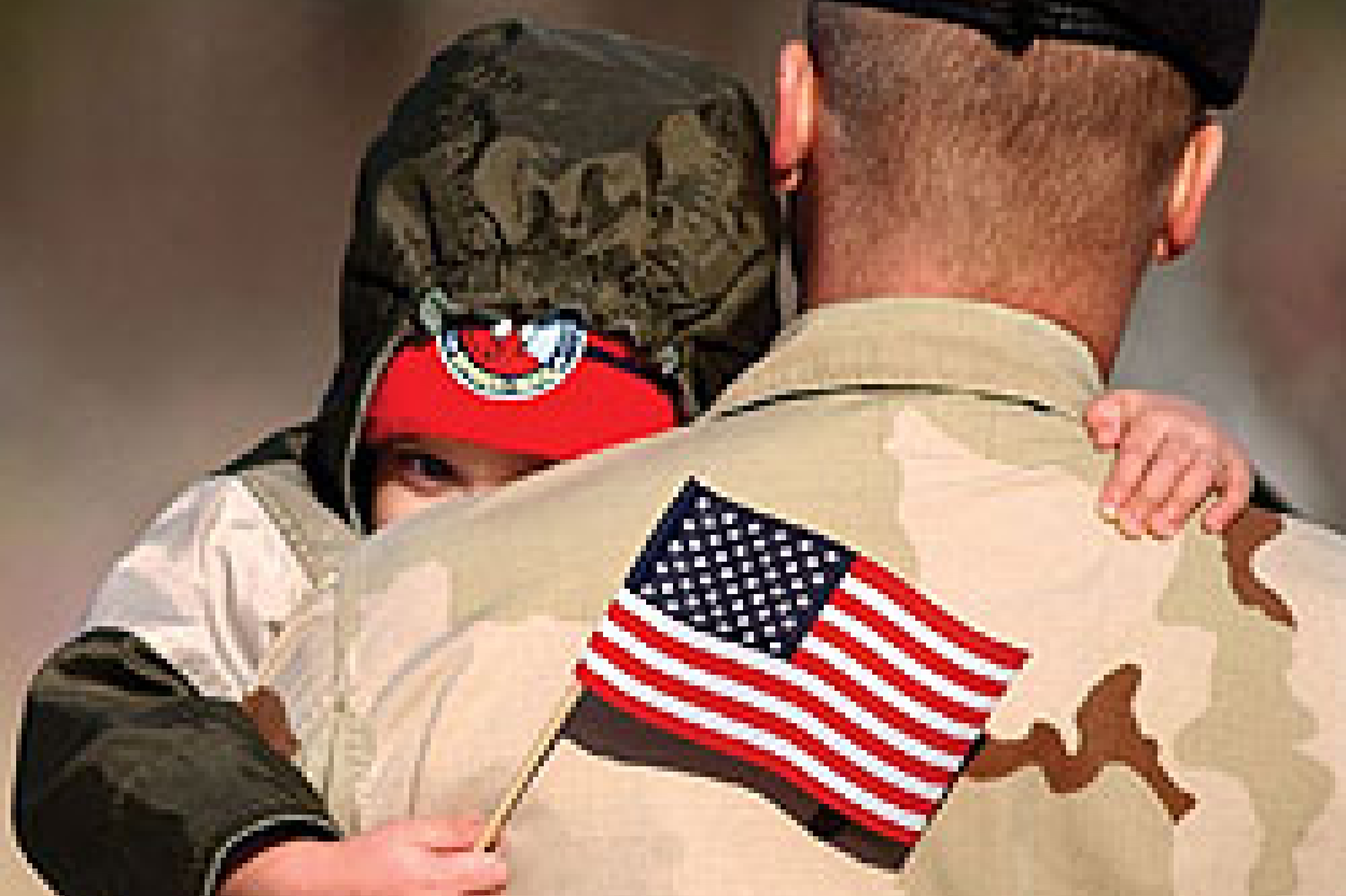 Male soldier in uniform holding his child, who is waving an American flag