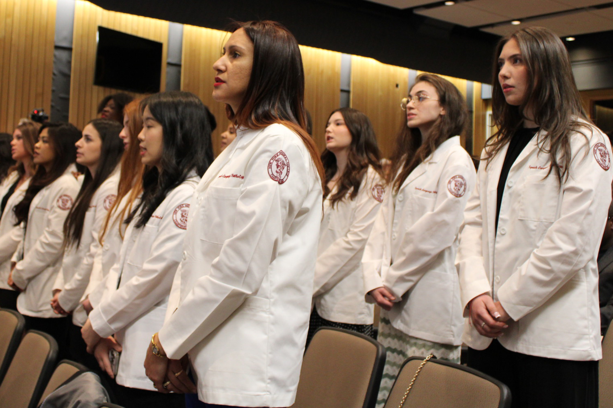 Group of SLP students standing in auditorium during white coat ceremony