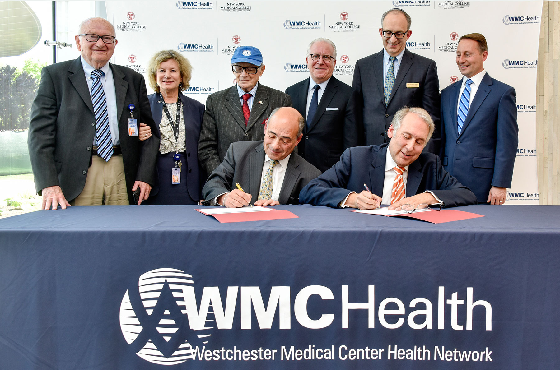 NYMC and Touro administrators leaning over table while official documents are being signed for NYMC to join Touro