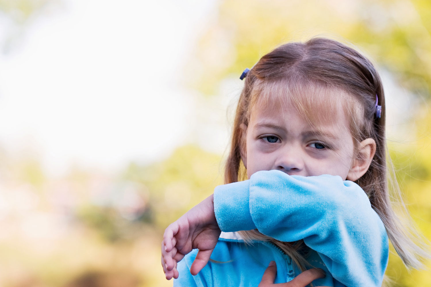 Young girl sneezing into elbow