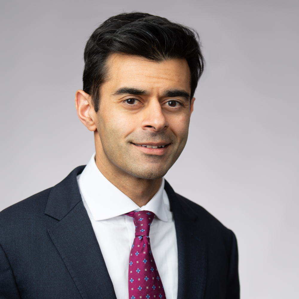 man with short dark hair wearing dark suit jacket with white shirt and maroon tie
